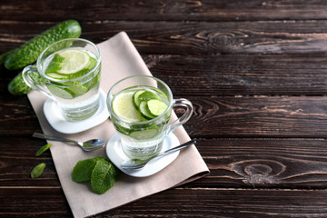 Delicious refreshing water with mint and cucumber in cups on wooden table