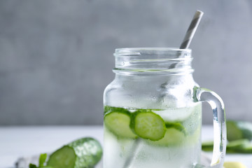 Delicious refreshing water with mint and cucumber in glass jar on blurred background, closeup