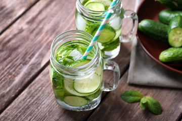 Delicious refreshing water with mint and cucumber in mason jars on wooden table