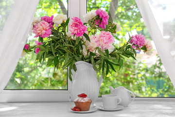 Delicious muffin and vase with beautiful peony flowers on windowsill