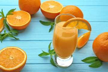 Glass of fresh juice and oranges on color wooden background