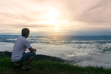 Naklejka na ściany i meble Man sitting morning sun in mist and fog scenery mountain background