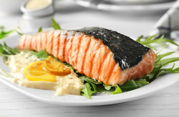 Plate with slice of delicious grilled salmon and fish sauce on table