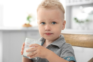 Cute little boy holding glass of milk with both hands in kitchen