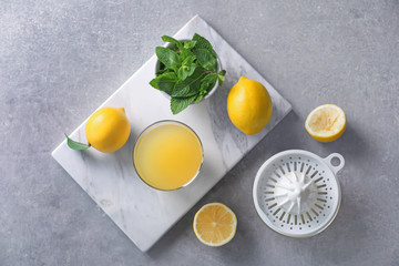 Composition with lemons, glass of juice, mint and plastic squeezer on grey background