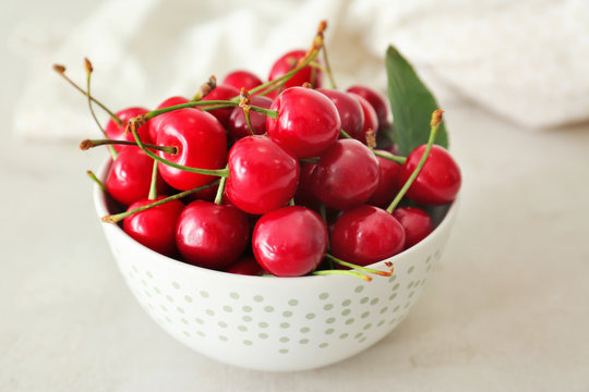 Ripe cherries in white ceramic bowl on light background
