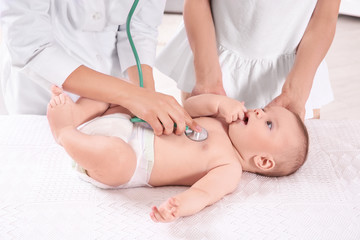 Doctor examining baby with stethoscope at home