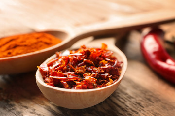 Red pepper flakes and chili powder in wooden spoons on table
