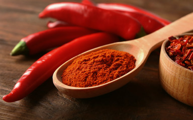 Red chili powder in wooden spoon and whole pepper pods on table