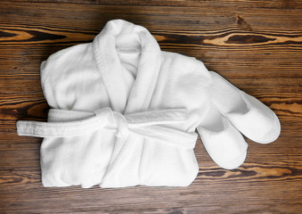 Folded bathrobe and bathing slippers on wooden background - obrazy, fototapety, plakaty