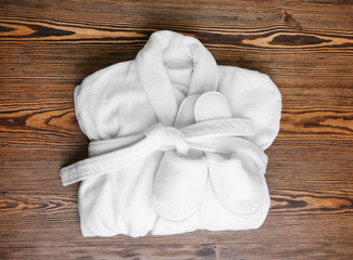 Folded bathrobe and bathing slippers on wooden background
