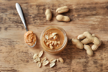 Jar and spoon with creamy peanut butter on wooden background