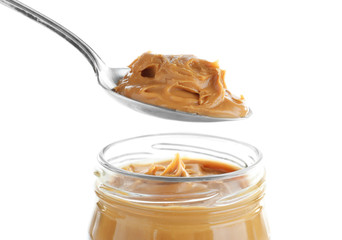 Creamy peanut butter in spoon and jar on white background