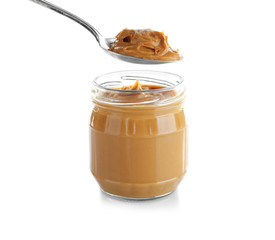 Creamy peanut butter in spoon and jar on white background