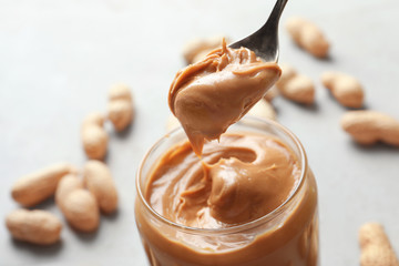 Creamy peanut butter in spoon and jar on blurred background