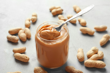 Creamy peanut butter in spoon and jar on table