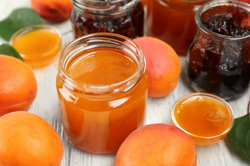 Apricot and berry jams in jars with ripe juicy fruit on wooden table