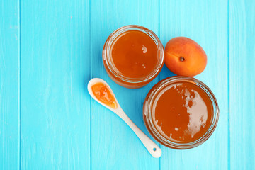 Apricot jam in jars with spoon and ripe juicy fruit on table