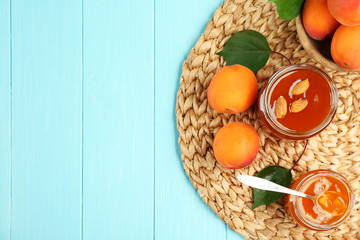 Apricot jam in jars with spoon and ripe juicy fruit on wicker mat