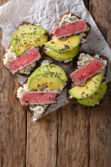 Super food: sandwiches with tuna steak in sesame, avocado and cottage cheese close-up. Vertical top view