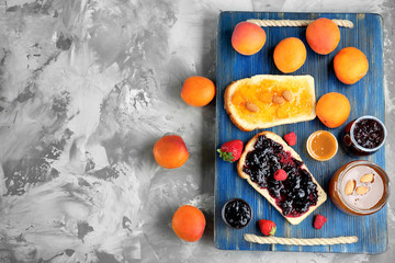 Two slices of bread with apricot and berry jams on wooden tray