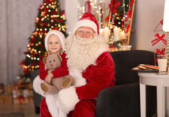 Fototapeta na wymiar Santa Claus and cute little girl with toy in room decorated for Christmas