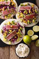 Mexican tacos with tuna, red cabbage, corn, avocado and onions close-up. Vertical top view