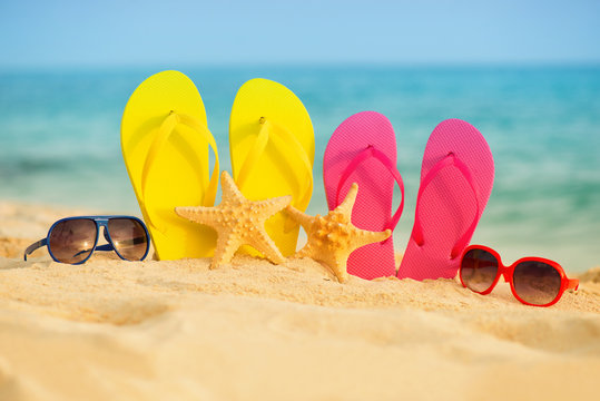 Glasses with yellow and pink sandals stand in the sand against the background of the sea