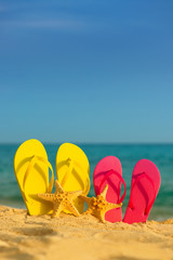 Sea-stars with yellow and pink sandals stand in the sand against the background of the sea.