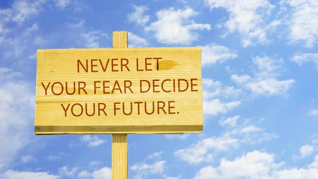 Never let your fear decide your future, Words on a wooden sign against time lapse clouds in the blue sky. 