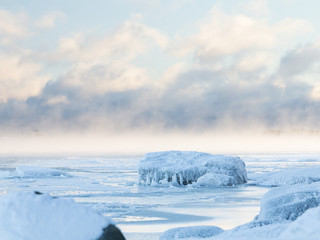 Magical backlit winter scenery with fluffy clouds, ice covered rock and smoke rising from the freezing sea.