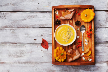 Vintage tray with autumn pumpkin soup decorated sesame seeds and thyme leaf in white bowl on rustic wooden table top view. Cozy lifestyle shot for halloween menu.