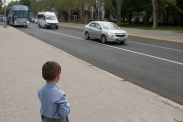 Little boy in a shirt looks at a city road with cars