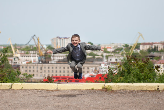 Happy handsome little boy in jacket jumping against the background of seaport