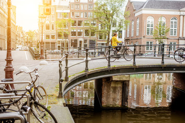 Obraz premium Cityscape view on the water channel and bridge with young woman riding a bicycle during the morning in Amsterdam city