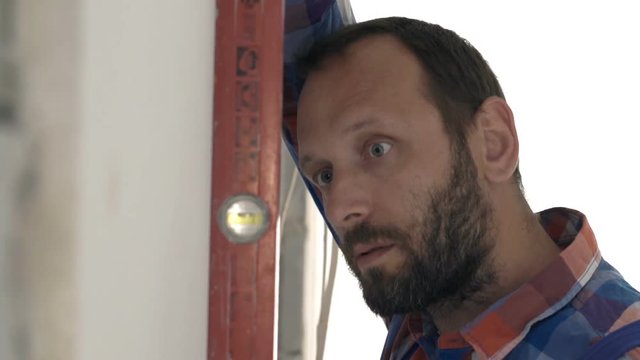 Male worker checking wall with level at new apartment 
