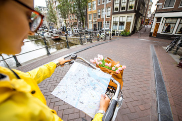 Fototapeta premium Kobieta na rowerze z mapą turystyczną na ulicy w mieście Amsterdam. Zobacz na ręce trzymając mapę