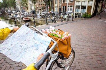Obraz premium Woman riding a bicycle with tourist map on the street in Amsterdam city. View on the hands holding map