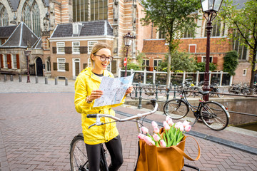 Obraz premium Portrait of a woman tourist in yellow raincoat standing with map and bicycle with Old church on the background in Amsterdam