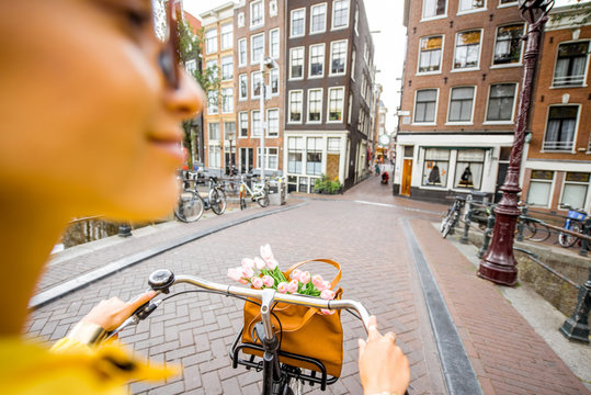 Woman riding a bicycle with bouquet of flowers on the street in Amsterdam city. View on the hands holding helm
