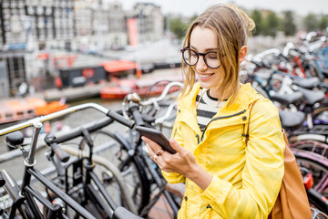 Fototapeta premium Young woman in yellow raincoat standing with phone on the bicycle multilevel parking in Amsterdam