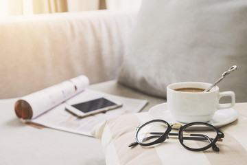Cup of coffee with glasses on sofa in living room