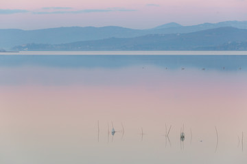 Fototapeta na wymiar A lake at dusk, with soft light, warm color, distant hills and mountains, fishing nets in the foreground