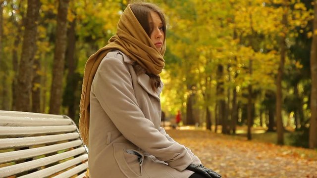 Woman in grey coat and scarf. She sitting on a bench and waiting for someone