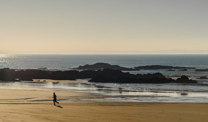 Fototapeta na wymiar Jogger läuft einsam über einen weiten Sandstrand der Sonne entgegen