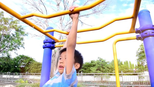 Slow motion of young asian Thai boy hang the yellow bar by his hand to exercise at the outdoor playground during the summer sunlight.