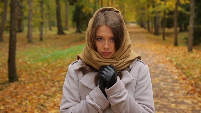 Beautiful sad caucasian woman in grey coat and knitted scarf in park at autumn