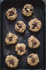 Freshly baked oatmeal raisin cookies with dark chocolate, cinnamon and nuts on old rusty cookie sheet. Table top view, vertical composition