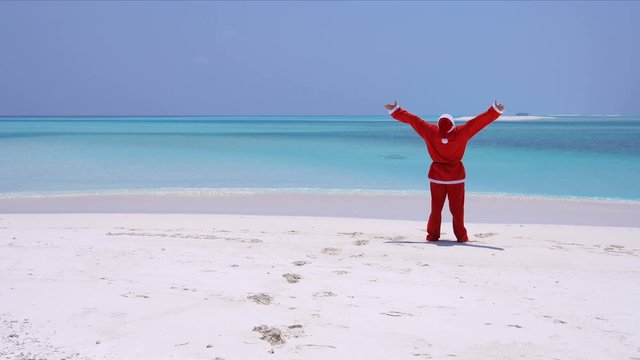 Man in Santa Claus Hat on beach and wag hands. Christmas vacation on Maldivian islands