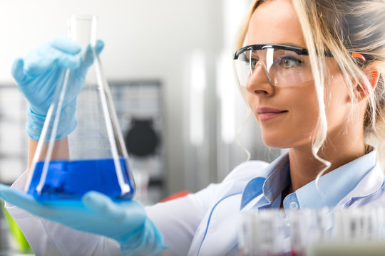 Young attractive female scientist holding a flask with blue liquid substance in the laboratory